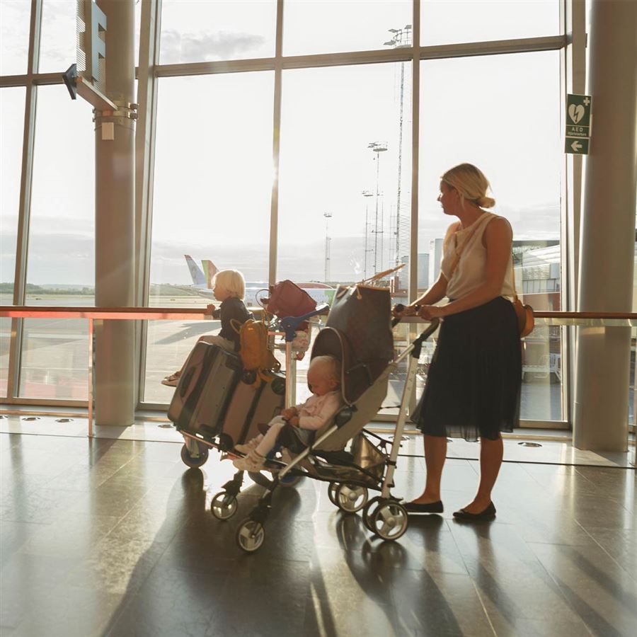 En mamma med sina två barn och en vagn full av väskor på en flygplats.