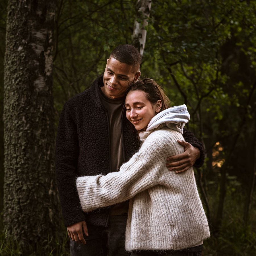 En kvinna och en man står och håller om varandra i en skogsglänta.