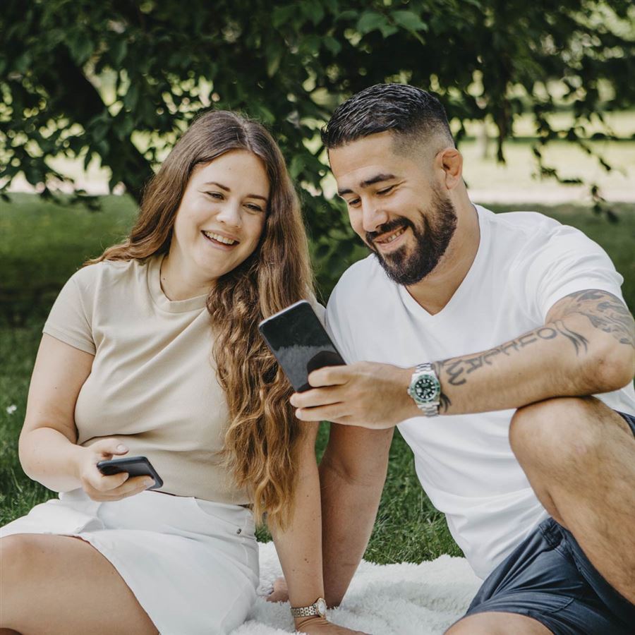 Par sitter på gräsmatta och kollar i en mobil