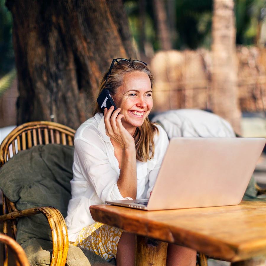Glad kvinna som sitter vid sin dator och pratar i telefon