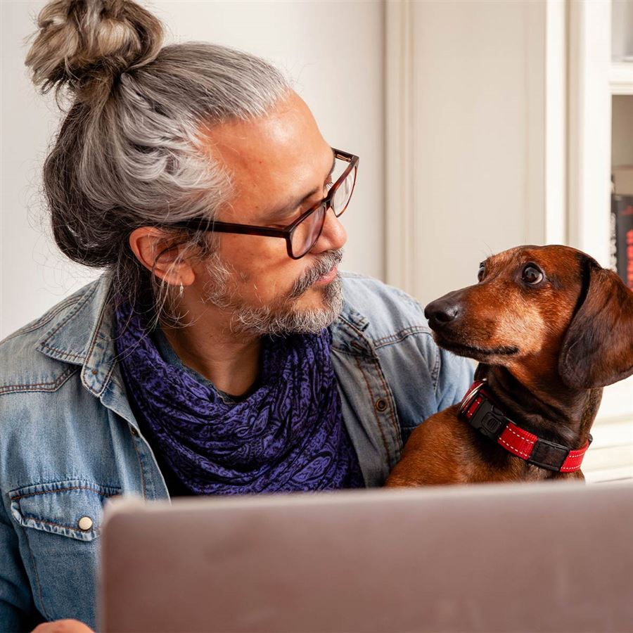 Man med en hund i knät framför dator