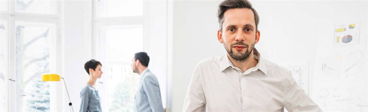 man på kontor med kollegor i bakgrunden