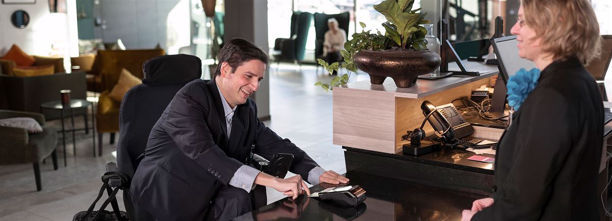 Man iklädd kostym betalar en nota i en hotellobby. 