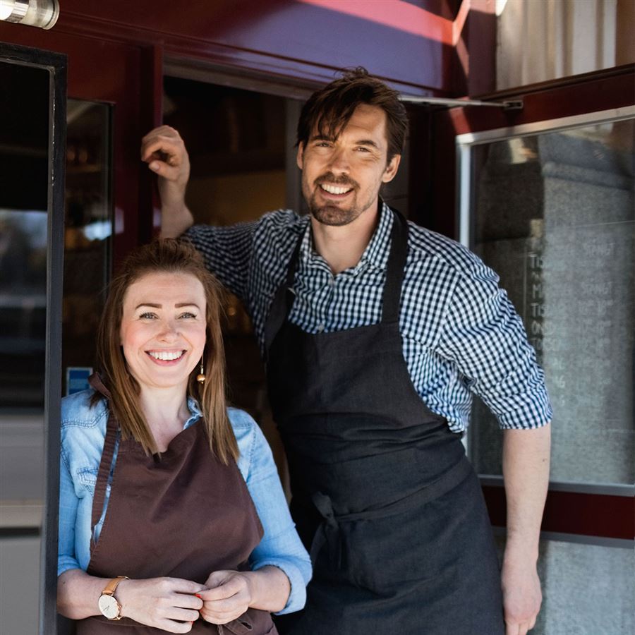 Två personer som jobbar på restaurang tittar ut genom en dörr