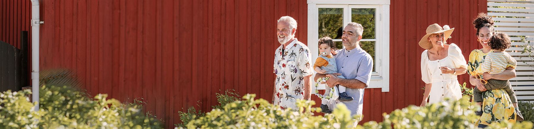 Solen skiner och en familj med små barn står framför en rödmålad stuga.