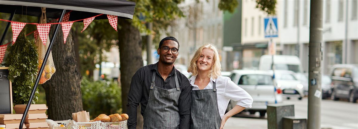 En man och en kvinna i förkläden står framför en foodtruck.