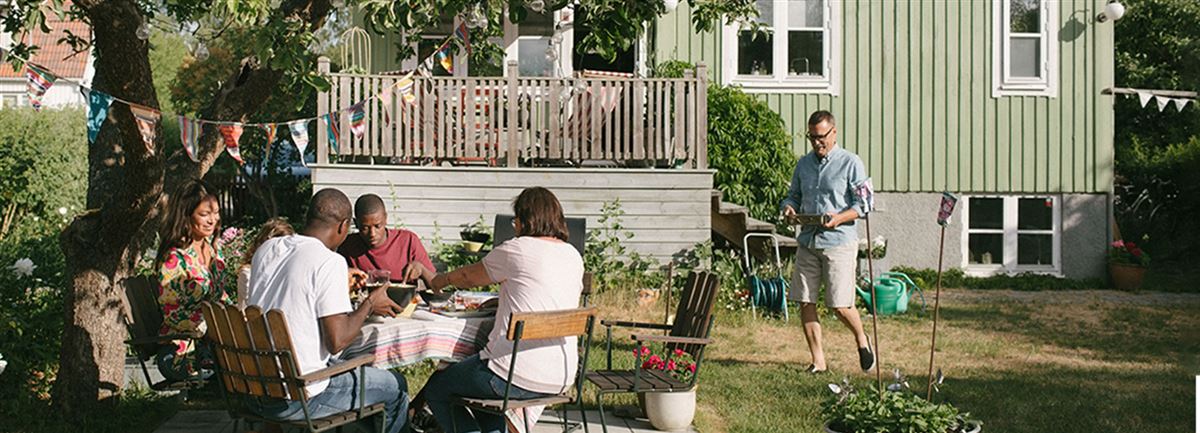 Familj sitter ute i trädgården och äter middag. Det är sommar. 