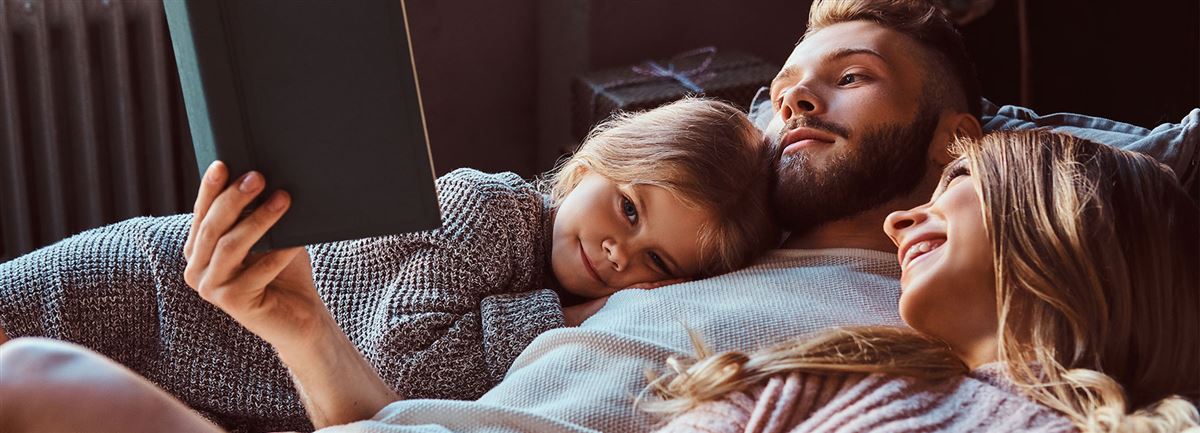 En familj som ligger i sängen och läser en bok.