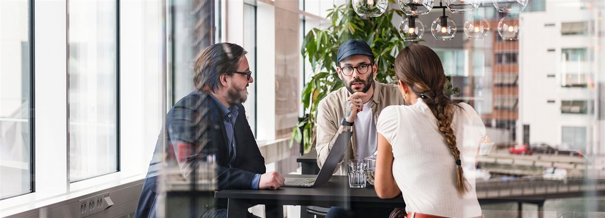 Tre personer som sitter runt ett bord och diskuterar.