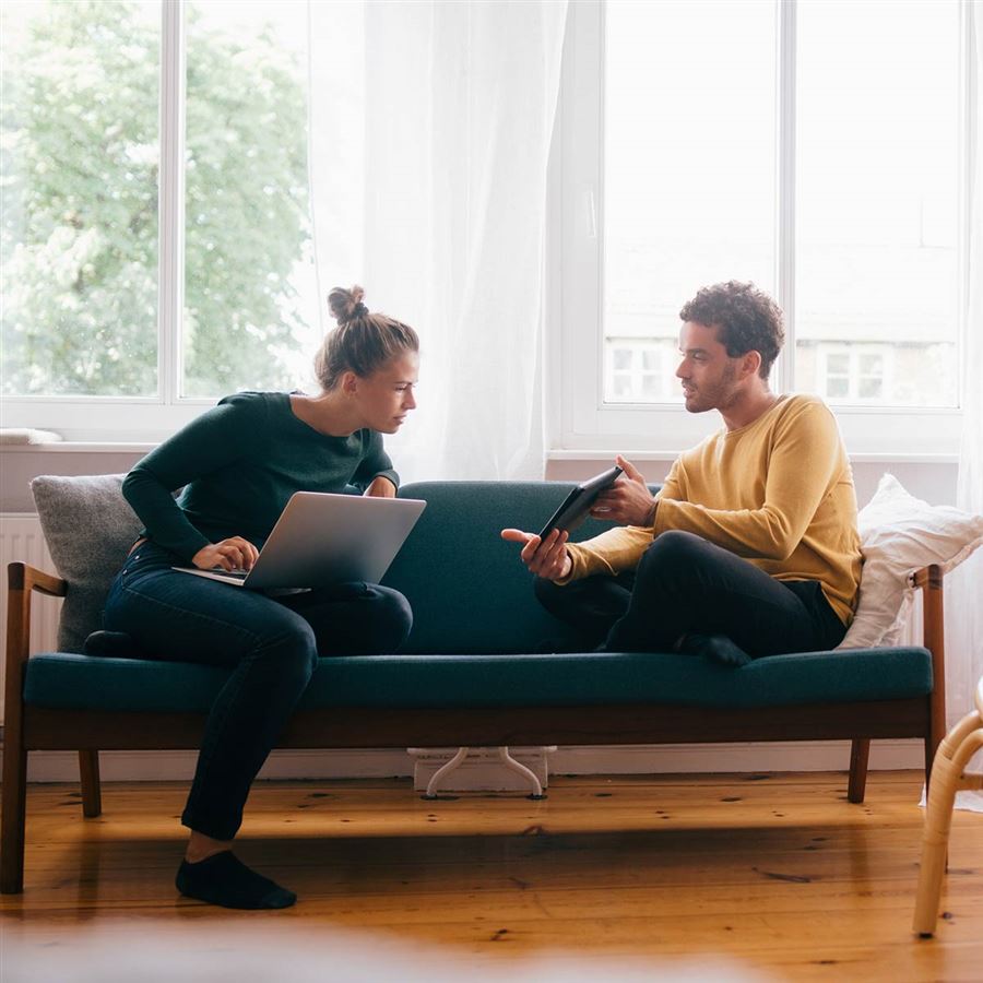 Ett par sitter i soffan och räknar på en budgetkalkyl för hemmets kostnader.