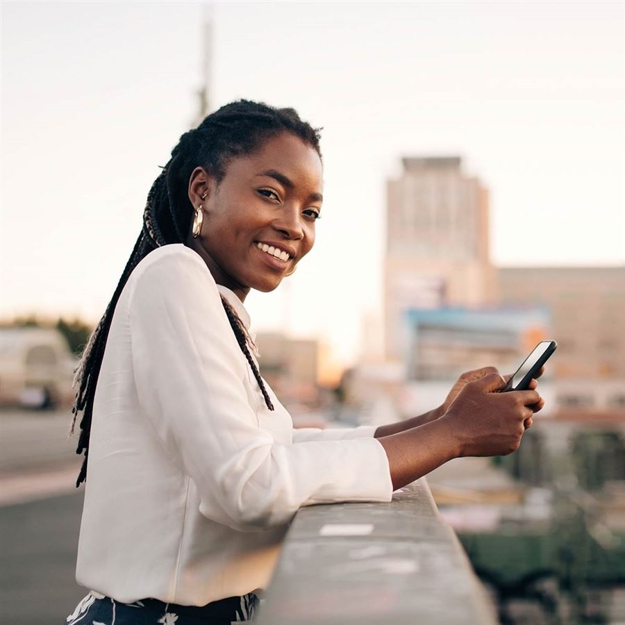 En leednde kvinna står på en bro med sin mobiltelefon i handen.