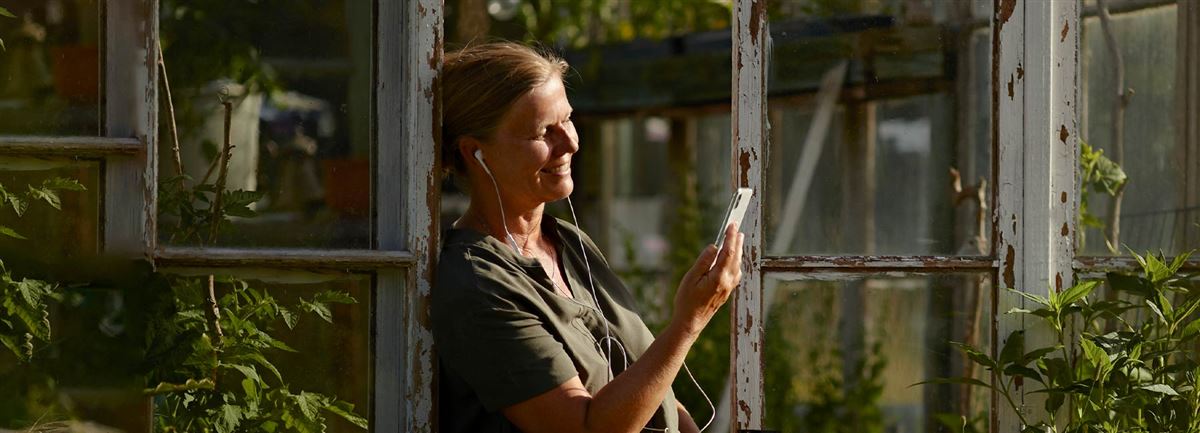 En kvinna har telefonmöte utanför sitt växthus.