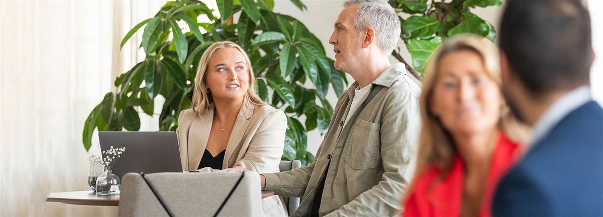En man och en kvinna sitter och pratar på ett kontor. I förgrunden ser man två andra personer i samtal. 