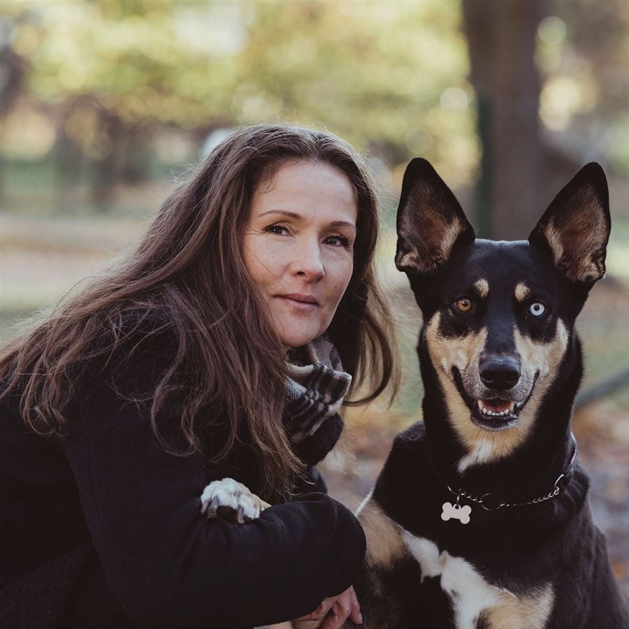 En kvinna sitter på huk bredvid sin hund. De är på promenad i skogen.