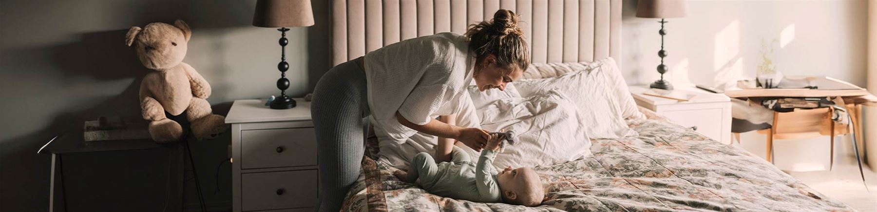 En mamma som gosar med sin bebis som ligger på sängen.