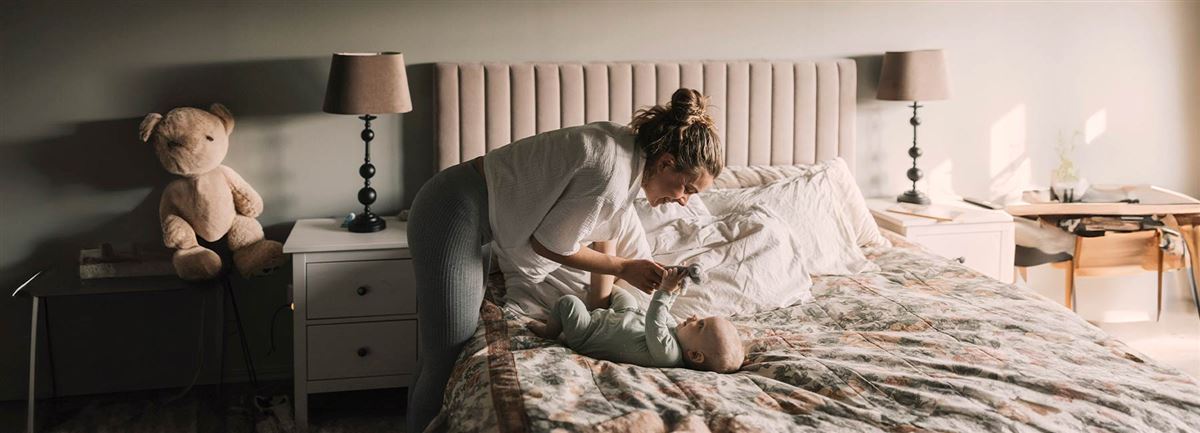 En mamma som gosar med sin bebis som ligger på sängen.