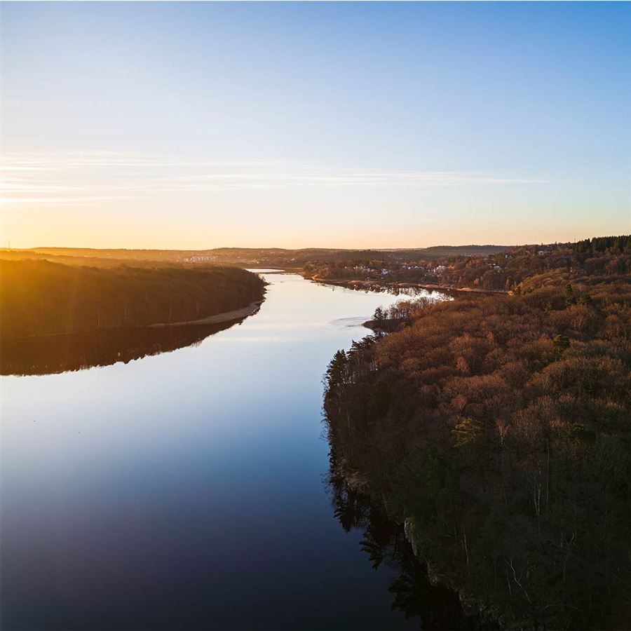 En flod rinner igenom ett landksap, solen går ner vid horisonten.