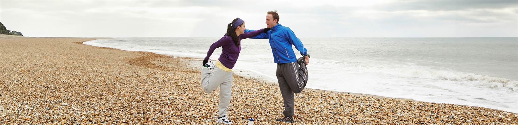 Par som stretchar på en strand efter en joggingtur