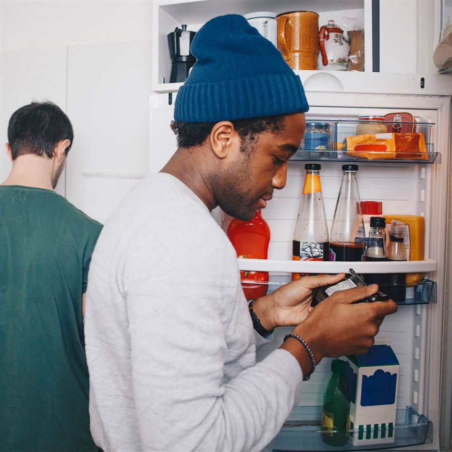 En ung kille som kikar in i ett kylskåp.