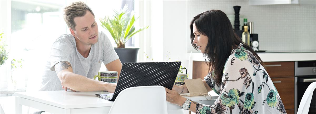 Man och kvinna sitter vid köksbordet och mannen tittar på datorskärmen.