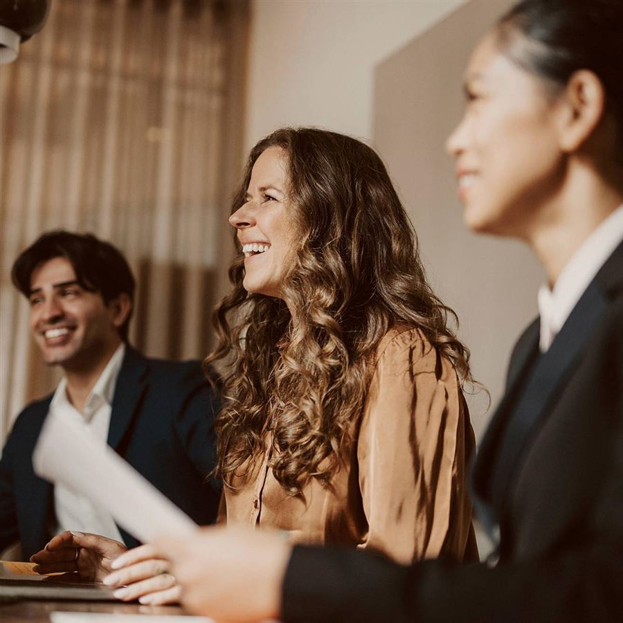 En man och två kvinnor sitter i möte. Det ser alla glada ut. 