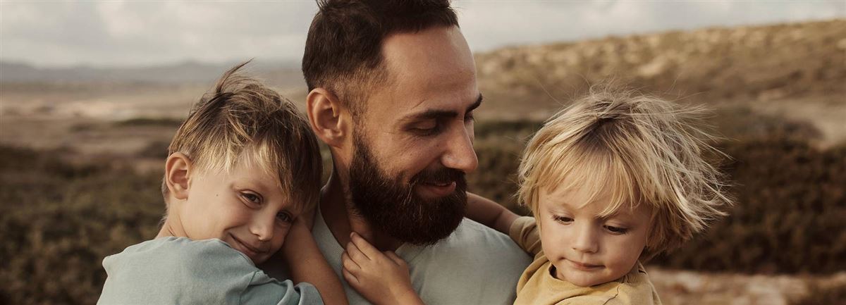 En man med två små barn i sin famn.