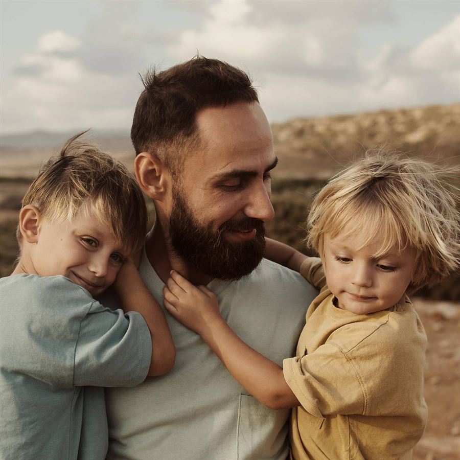 En pappa med sina två barn i famnen.