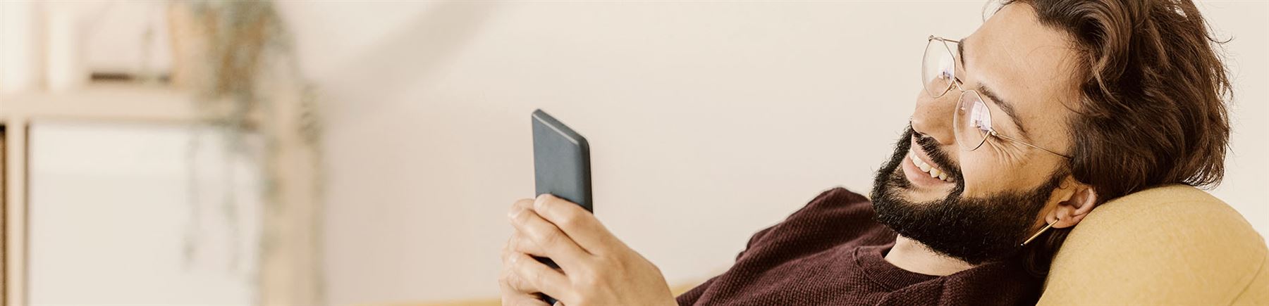 Man som sitter i soffa och tittar på sin mobiltelefon.