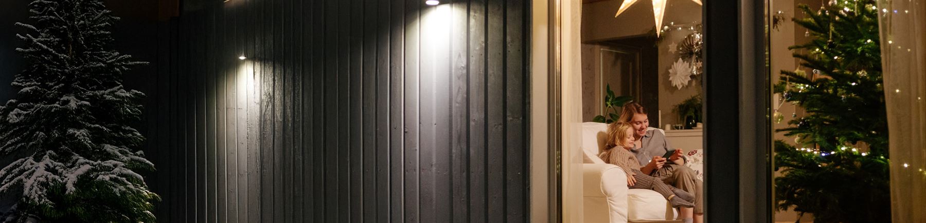 Mor och dotter sitter i soffan framför julgran och julklappar.