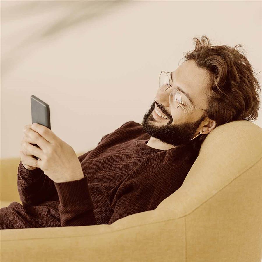 Man som sitter i soffan och tittar på sin mobiltelefon.