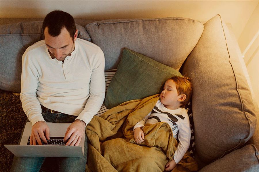 Pappa med dator i soffan bredvid sin son.