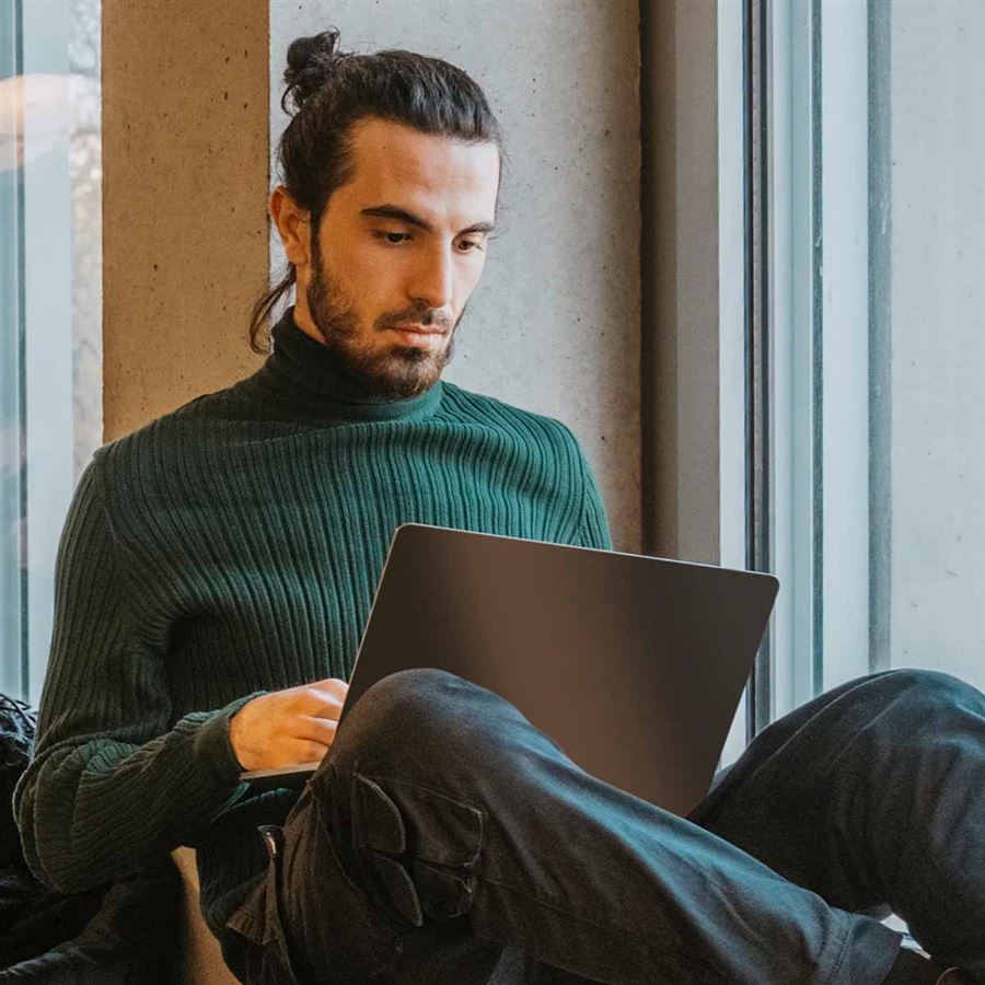 Man i fönster läser om csn-lån bakom sin laptop.