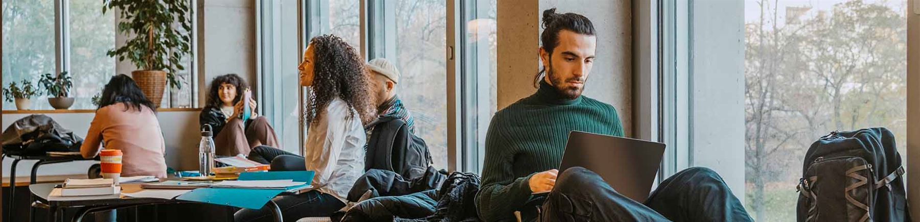 Man i fönster läser om csn-lån bakom sin laptop.