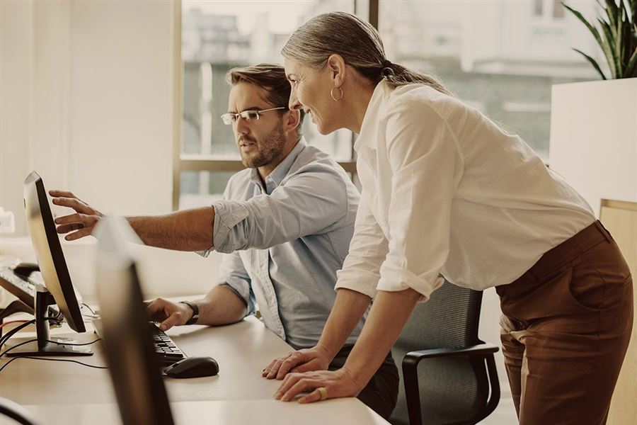 Två kollegor diskuterar aktiemarknaden och tittar på en datorskärm.