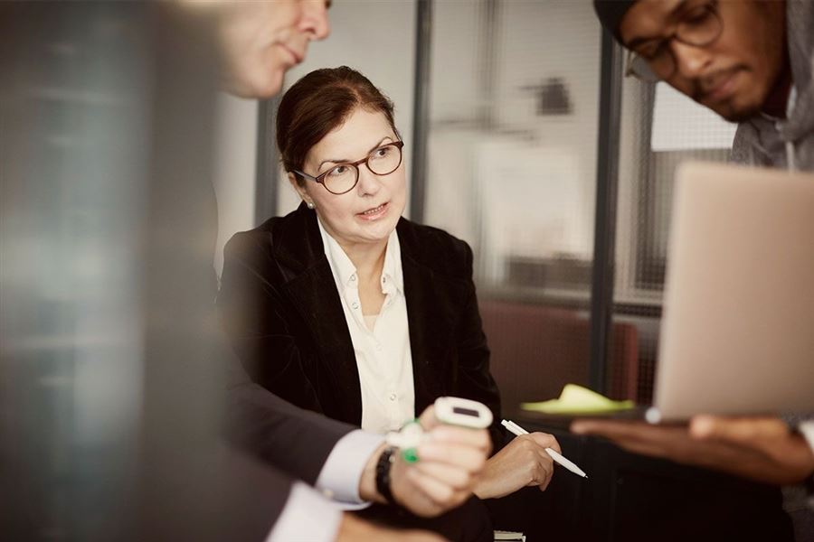 En kvinna iklädd kostym tittar på en laptop tillsammans med två kollegor.