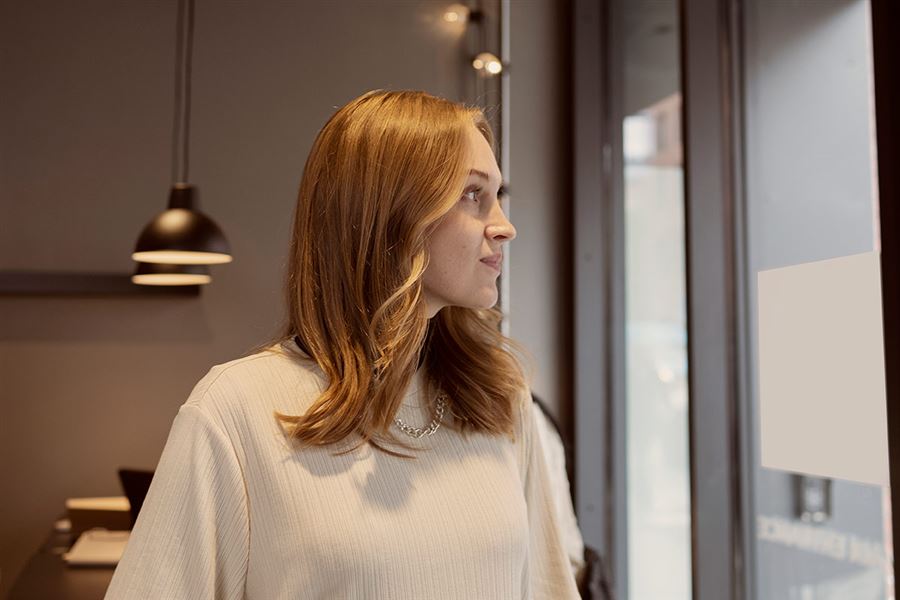 Kvinna på kontor ser ut genom ett fönster. Hon funderar på att öppna ISK.