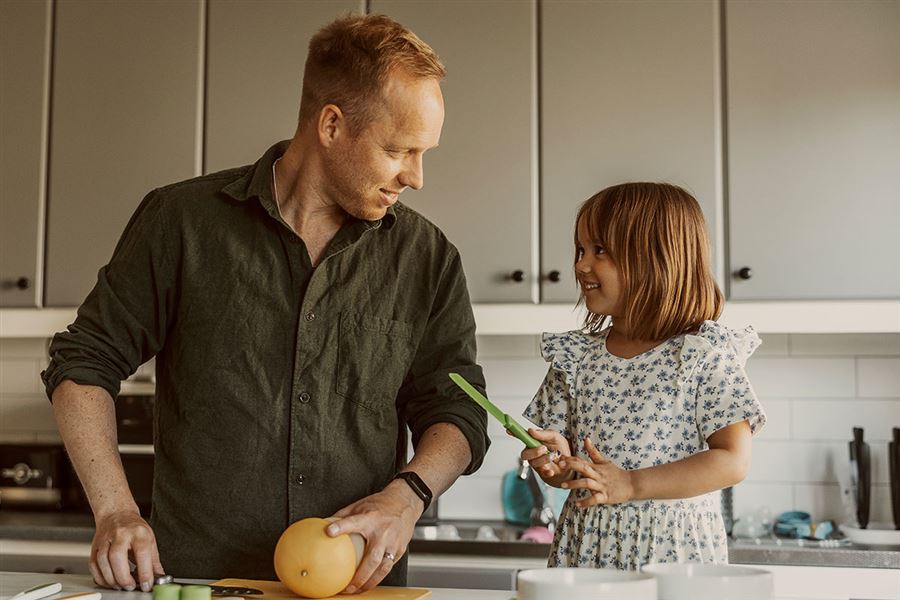 En man står i ett kök med sin lilla dotter. De förbereder mat tillsammans. 