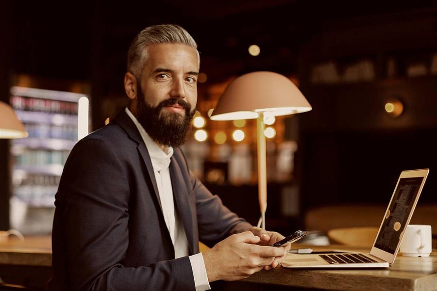 Affärsman sitter i en kontorsmiljö med sin mobil och laptop.