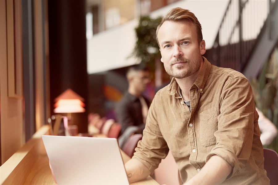 En man sitter framför sin laptop på ett café.