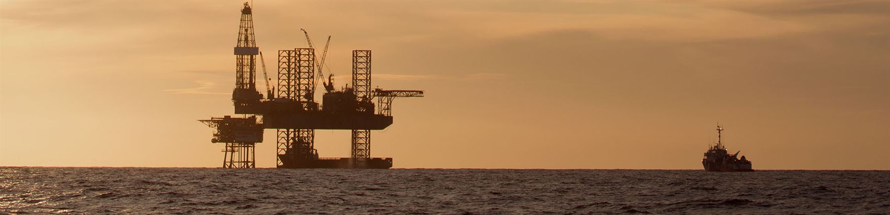 En oljerigg och ett oljefartyg i solnedgång.