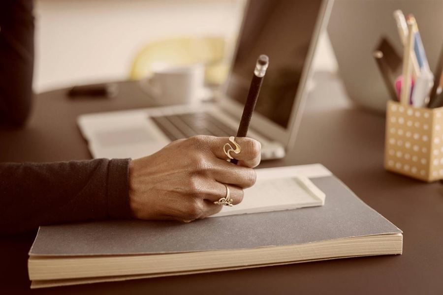 Bild på en hand som håller i en penna och fyller i ansökan.