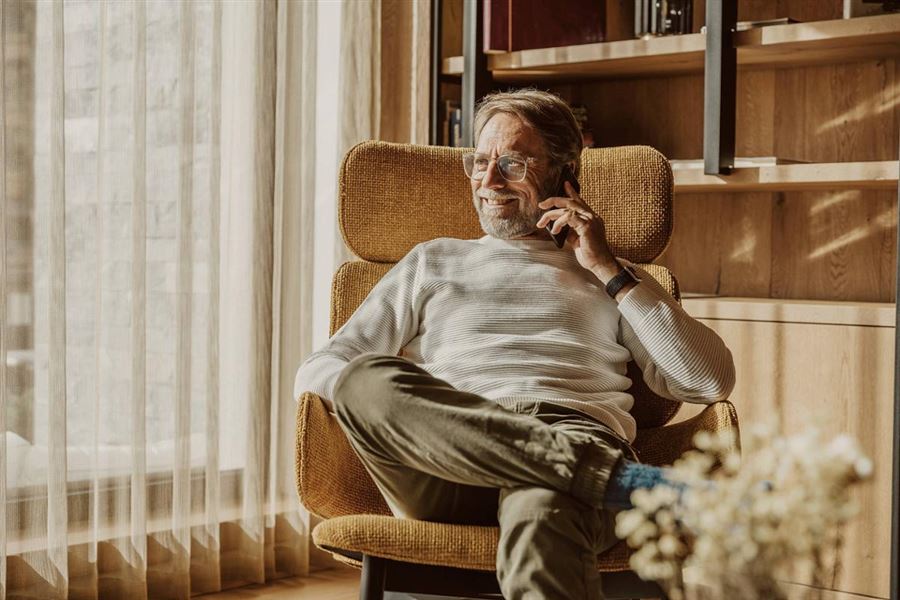 En man sitter i en fotölj och pratar i telefon.