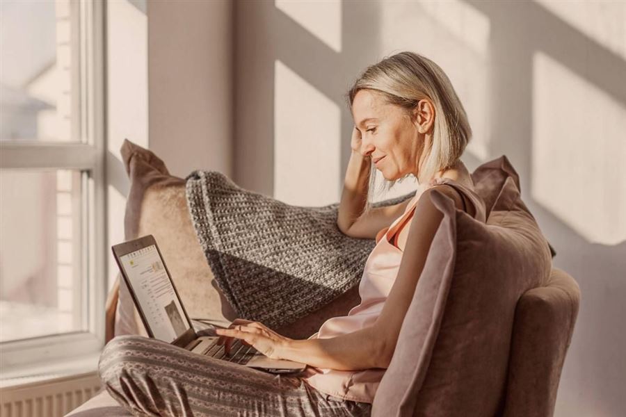 En kvinna sitter i ensoffa med en laptop i knät.