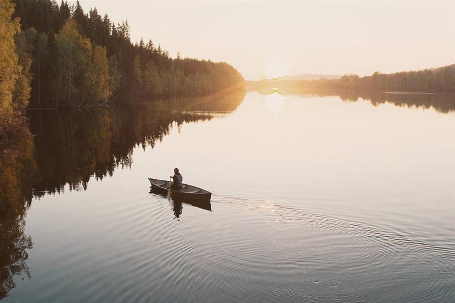 En kvinna paddlar kanot på en stilla sjö i solnedgång.