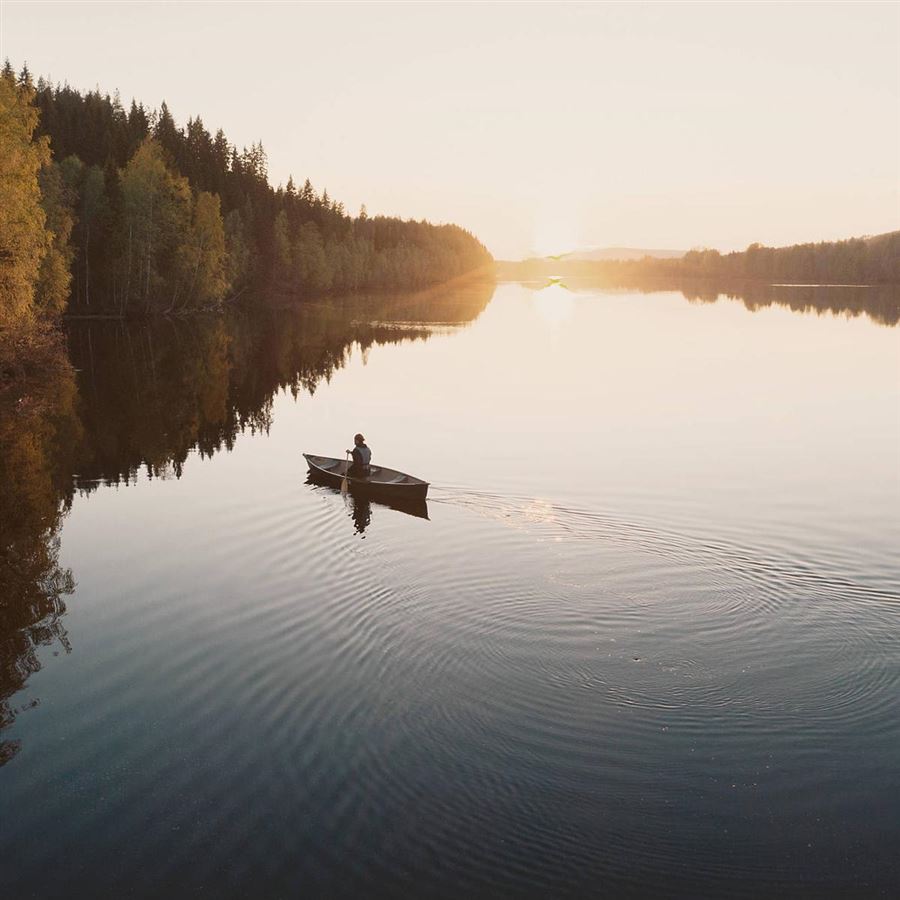 En kvinna paddlar kanot på en stilla sjö i solnedgång.