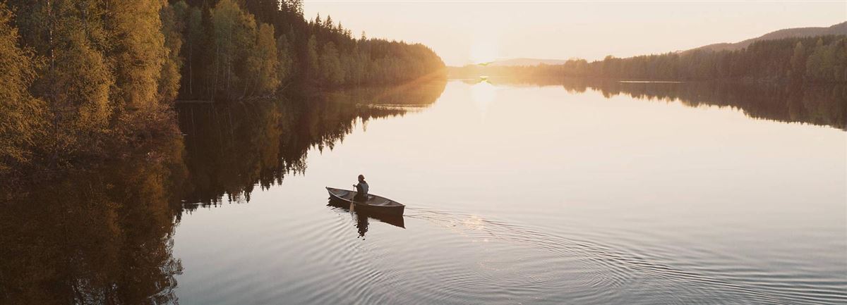 En kvinna paddar kanot på en stilla sjö i solnedgång.