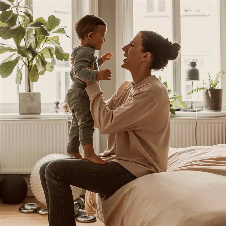 Mamma som sitter med sitt barn på sängen.