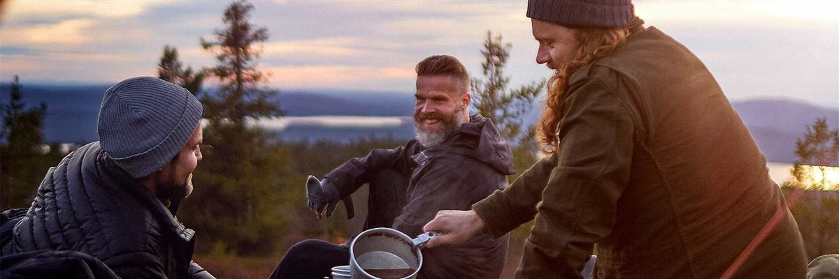 Tre män sitter och dricker kaffe i skogen