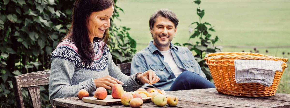 Kvinnna och man sitter i trädgården och rensar äpplen.