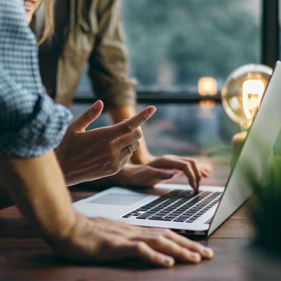Two people is leaning over a laptop. You can only see ther hands. 